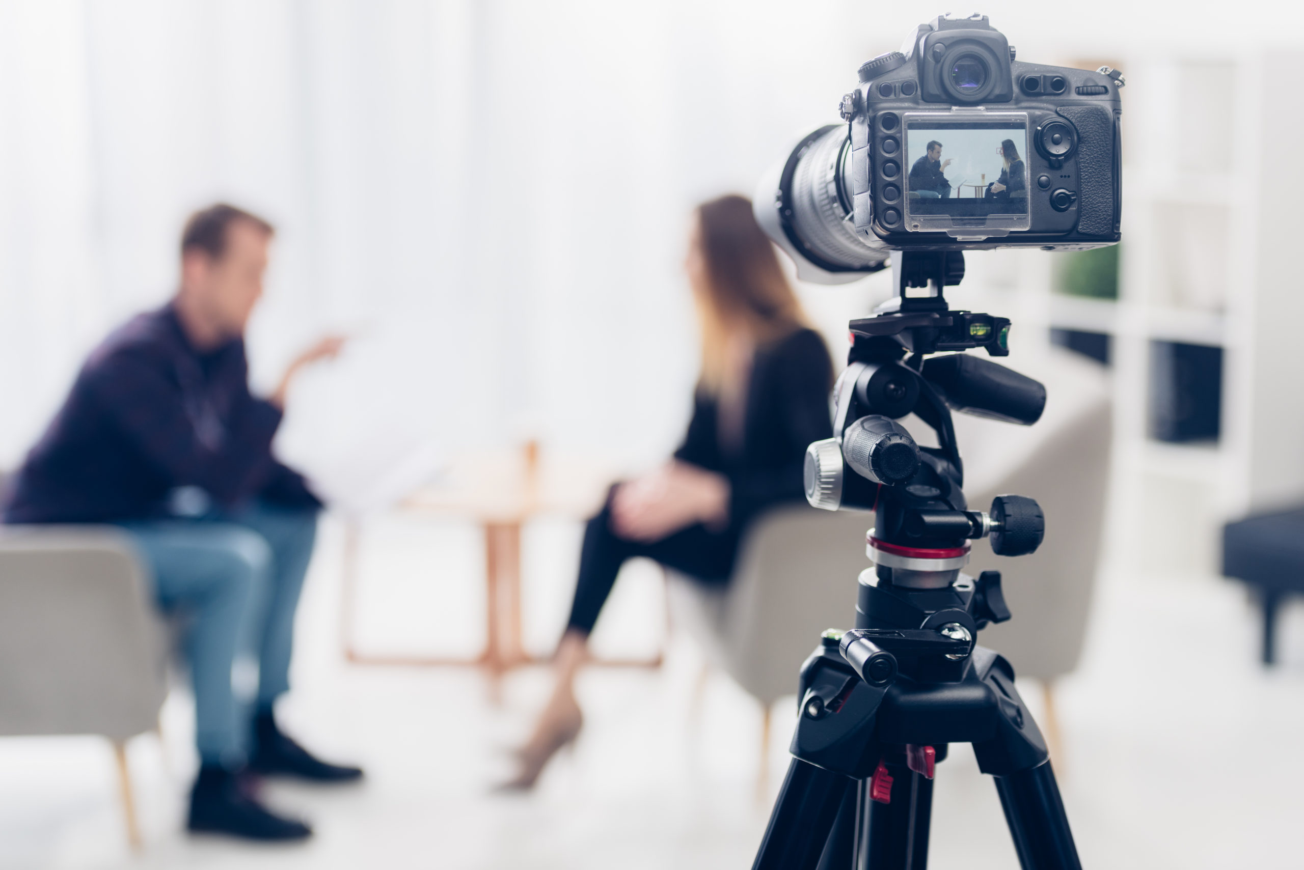 businesswoman in suit giving interview to journalist in office, camera on tripod on foreground